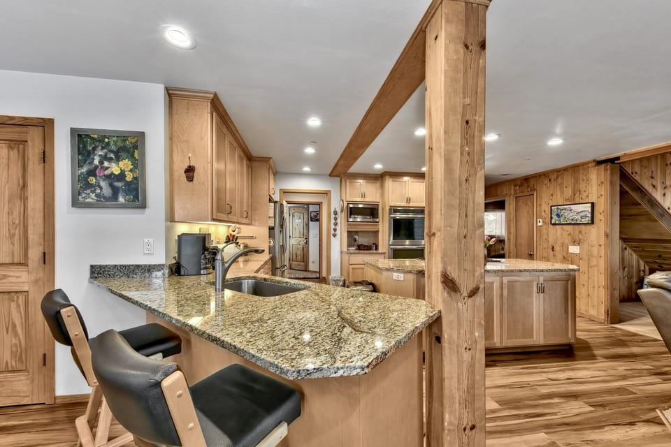 Kitchen bar with granite countertops, black cushioned stools, wooden cabinetry, and recessed ceiling lights.