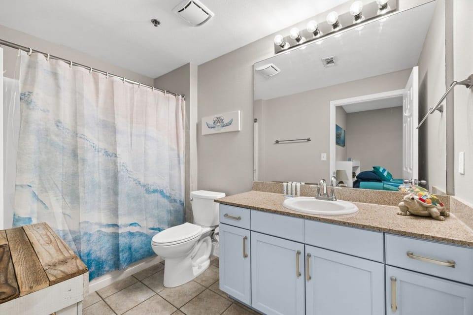 Freshen up in this bright bathroom featuring a granite vanity, large mirror, toilet, tub-shower combination, and coastal-inspired décor.