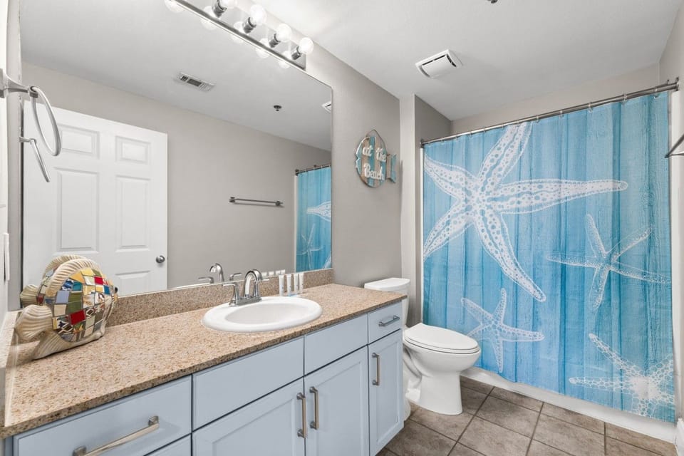 Freshen up in this bright bathroom featuring a granite vanity, large mirror, toilet, and tub-shower combination with coastal décor.