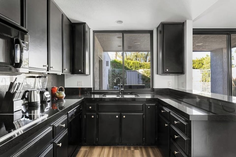 Sunlit kitchen with dark granite counters, black cabinetry, stainless sink, and garden-view windows — fully stocked for group cooking