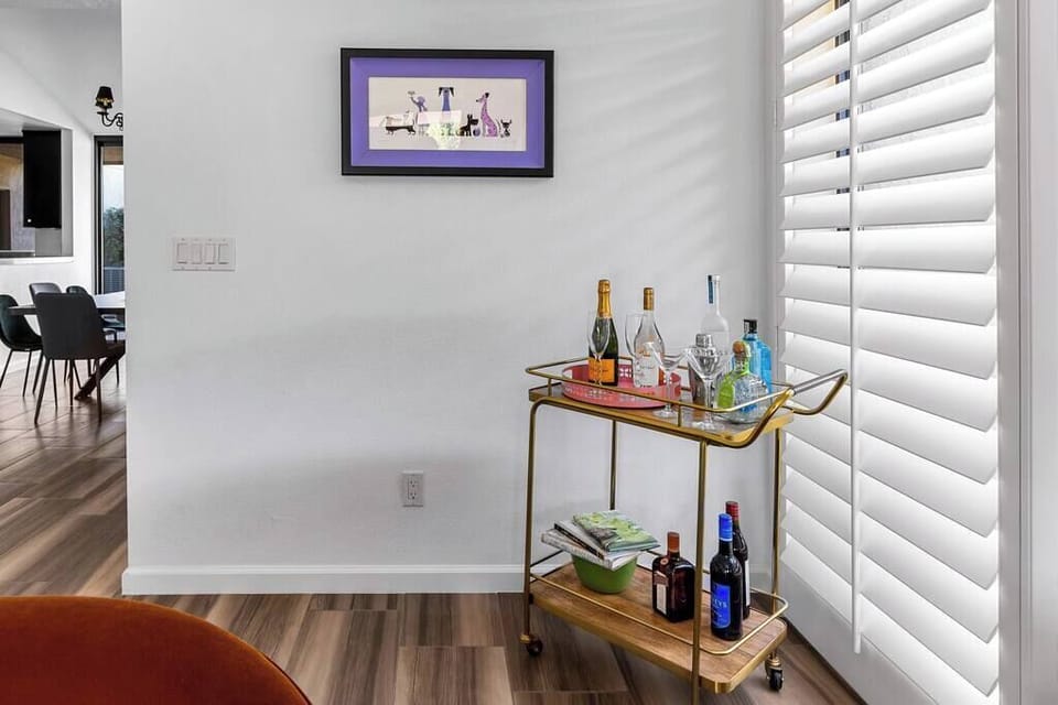 Gold bar cart stocked with bottles and glassware by plantation-shuttered window — happy hour starts at check-in