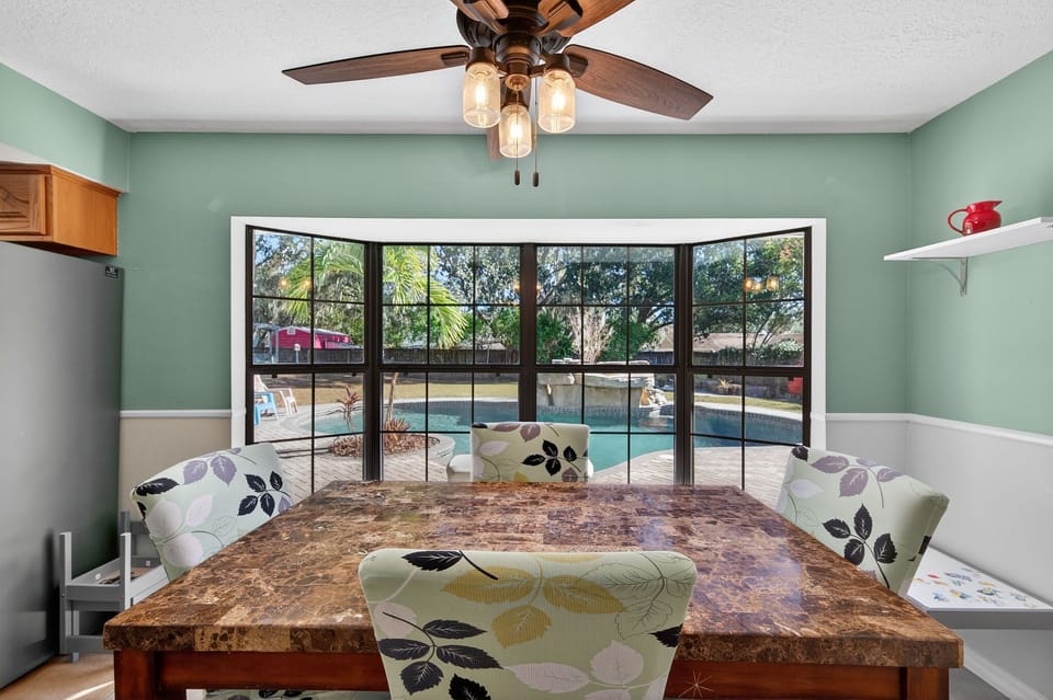 Dining area with large table and pool views through expansive windows.