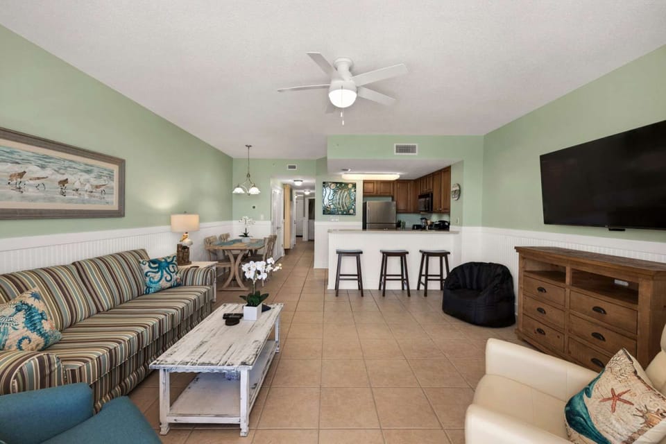 open living area with striped sofa, kitchen bar seating, and a wall-mounted television