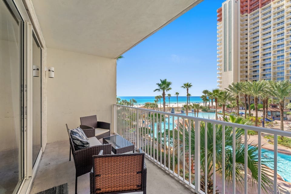 Relax on the balcony with views of the pool, palm trees, and ocean beyond.