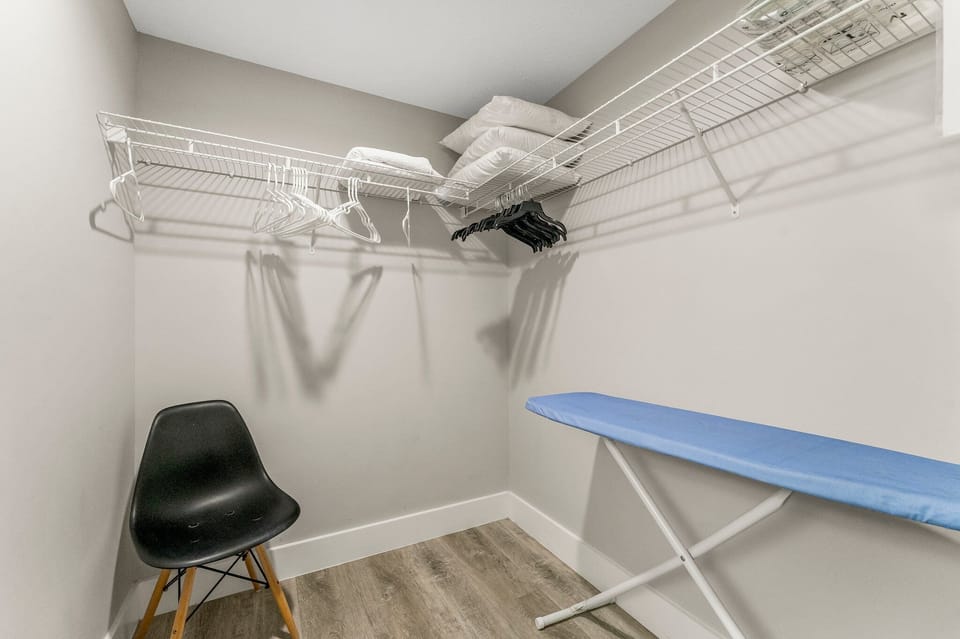 Closet space with wire shelving, hangers, and an ironing board for guest convenience.