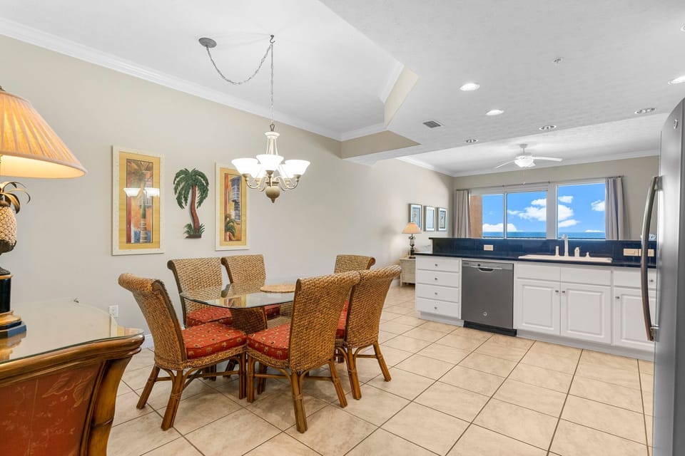 Dining area with wicker chairs and a view of the kitchen and large window.