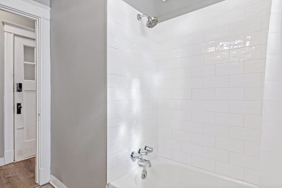 The bathroom tub-and-shower combination includes a white tub, white subway-tile surround, chrome showerhead and faucet, and curtain at the edge of the frame.
