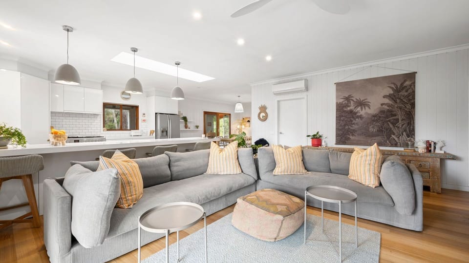 With its soothing neutral tones of elegant white walls, cosy grey couches, and accents of soft orange pillows, the living room is as welcoming and calming as it can be.