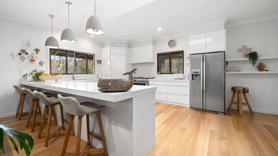 All-white full kitchen with a long benchtop and 3 pendant lights, giving the place a modern and elegant appeal. 