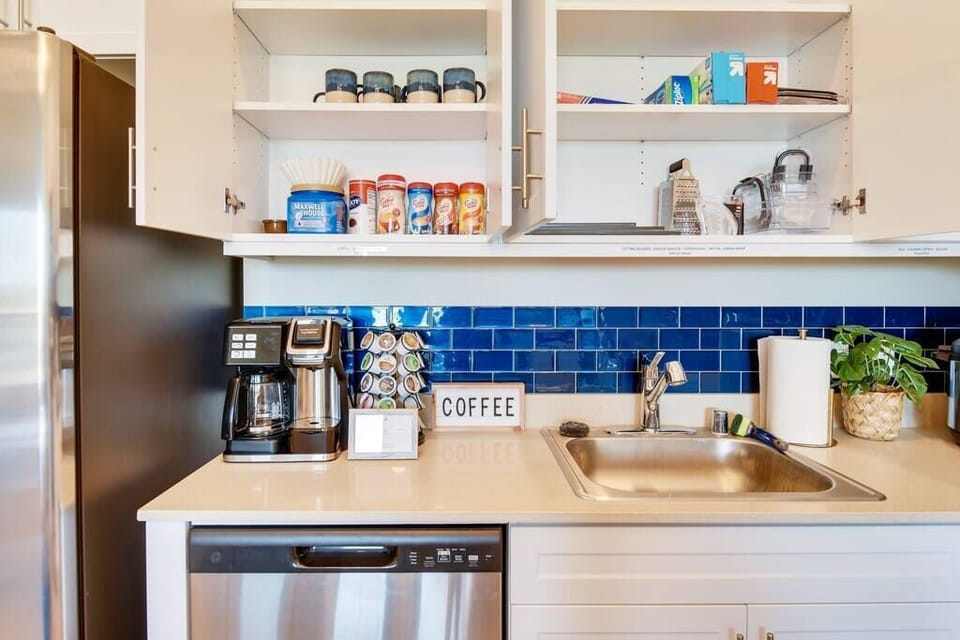 [Kitchen] - dual coffee machine with drip and k-cup functionality; variety of coffees, teas, and hot chocolate; variety of flavored creamers; sugar; mugs; Saran Wrap; tin foil; ziplock bags; Tupperware; cheese grater; measuring cup; cutting boards