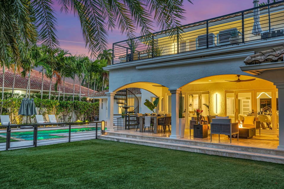 The covered patio contains a dining table for eight and a sitting area with TV and a fire pit. The backyard turf holds an outdoor kitchen equipped with bar seating for six and a grill.