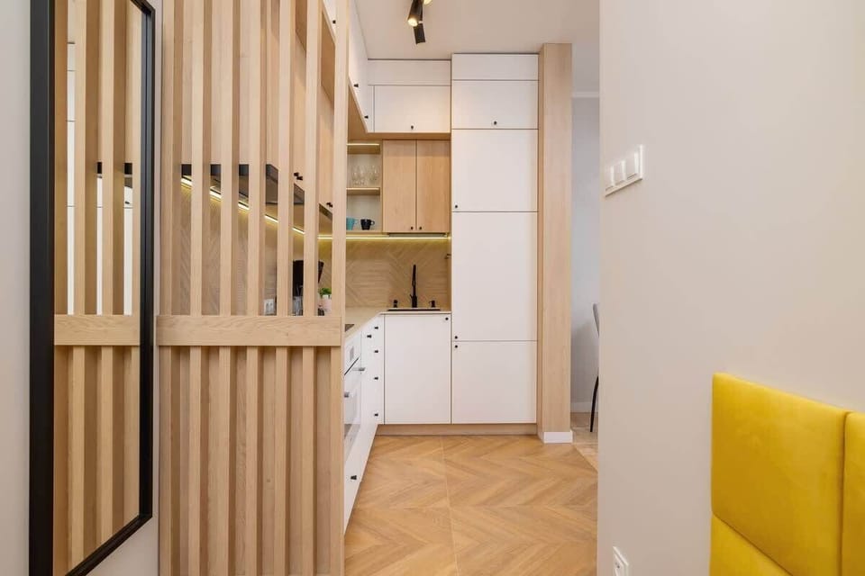 A hallway with wooden room dividers, minimalist decor, and a yellow accent chair, creating a warm and contemporary transition space.
