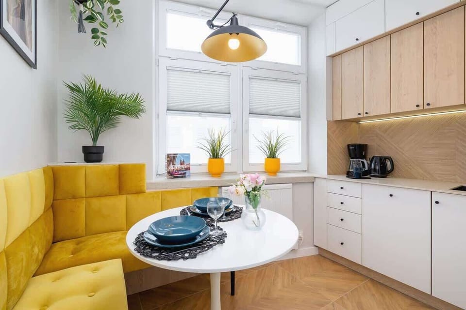 A bright dining nook with a round white table, vibrant yellow cushioned seating, and minimalist wooden cabinets, creating a cheerful and modern dining space.
