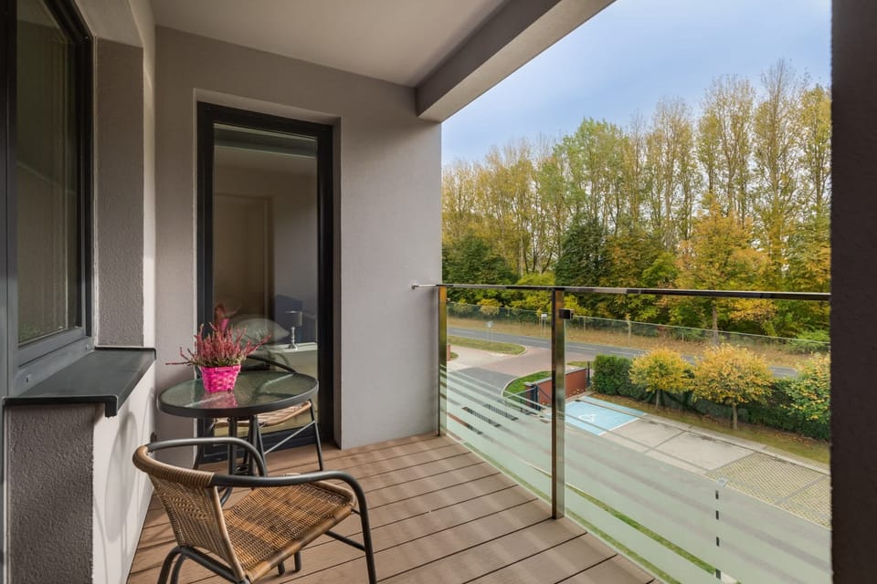 A private balcony with a table and chairs, overlooking a peaceful green area, ideal for relaxing outdoors.
