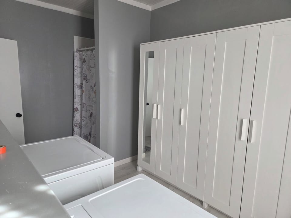 Laundry room with shower, iron and ironing board, card table and folding chairs.