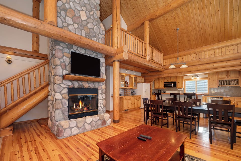 - Cozy log cabin living room with stone fireplace glow   - Open concept design with vaulted wooden ceilings   - Relax by the fire after a day exploring mountain trails