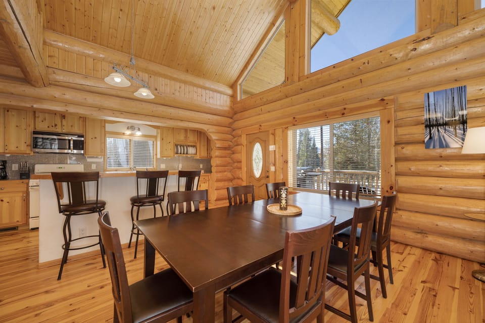 - Large dining table with cabin wood interiors charm   - Bright natural light through tall cabin windows   - Perfect spot to share mountain meals with family