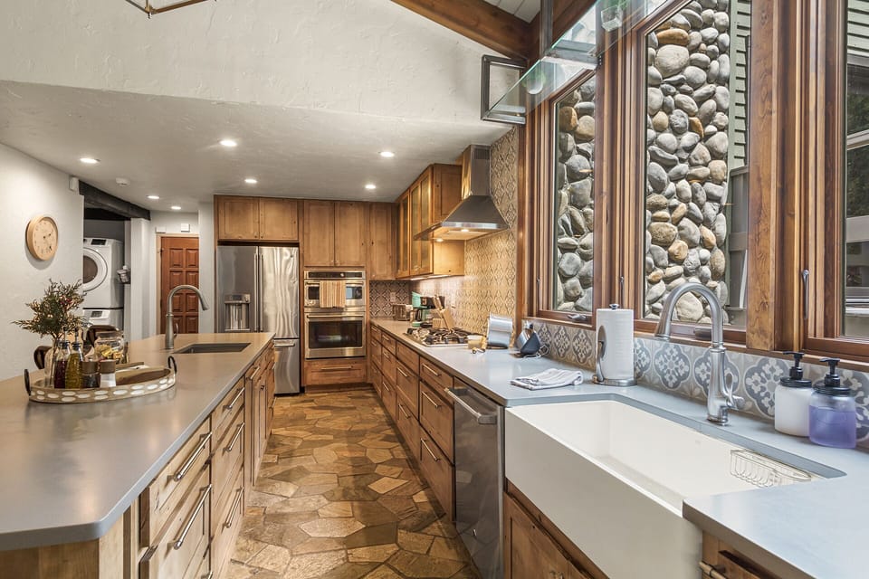 Gathering Island Kitchen — Stainless appliances, double sinks, and a generous island with seating—perfect for sipping wine, sharing stories, and watching the creek drift by. 🍷🏞️