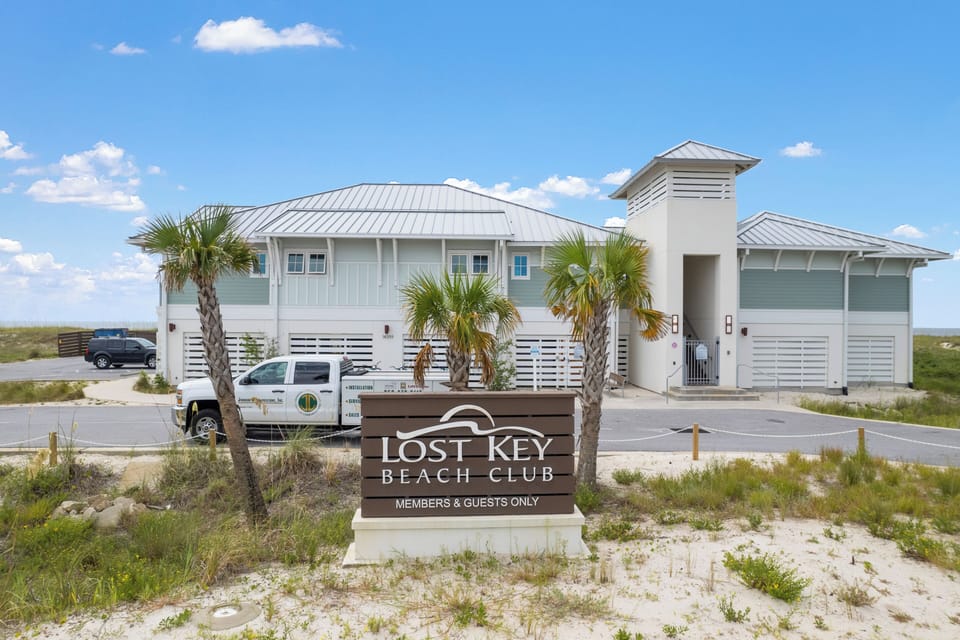 The Lost Key Beach Club welcomes members and guests with its coastal architecture, palm-lined entrance, and convenient parking, situated in a natural beachside setting.