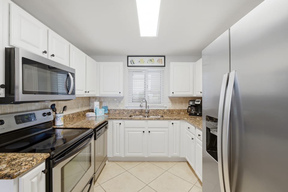 Sandy Key 318- Your fully equipped kitchen features crisp white cabinetry, granite countertops, and stainless steel appliances ready for your vacation meals.