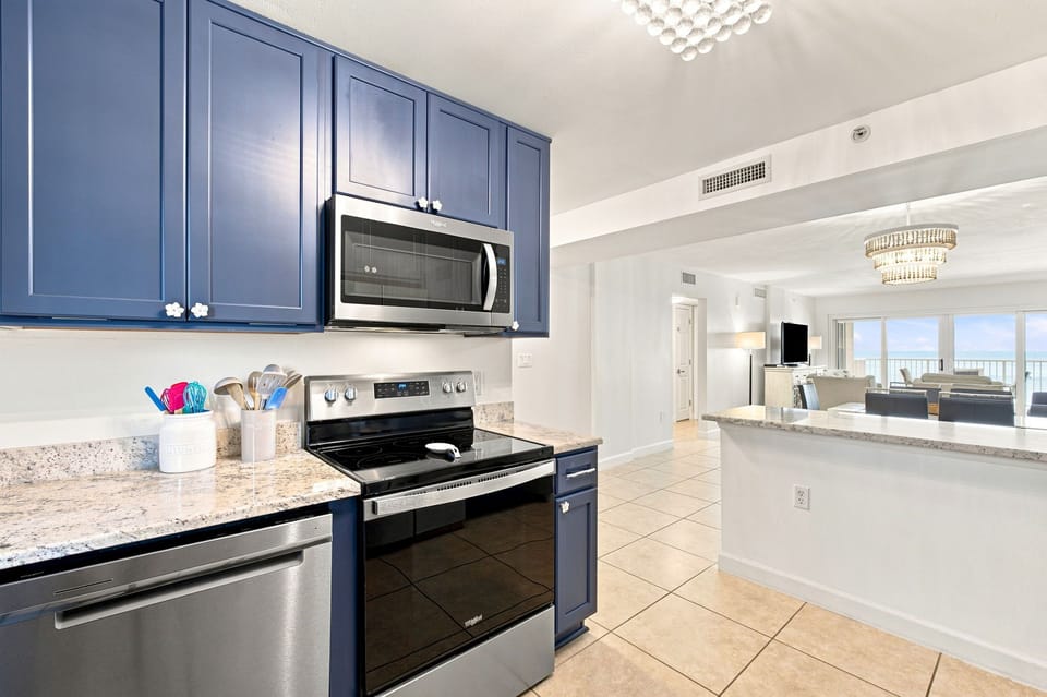 Sandy Key 411- Your fully-equipped kitchen features sleek navy cabinetry, granite counters, and stainless appliances—perfect for preparing meals while soaking in that stunning ocean view just beyond the living area.