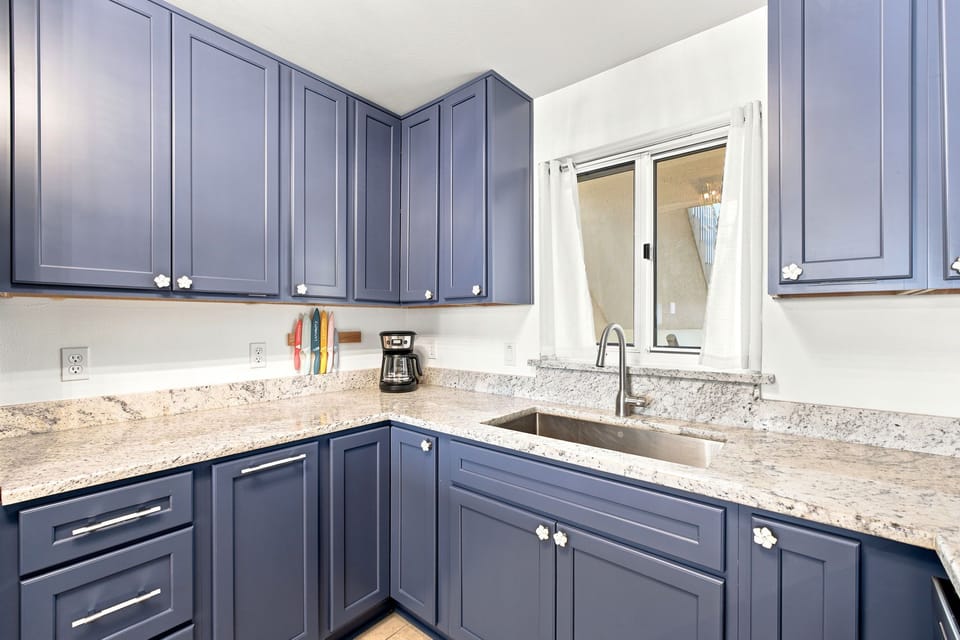 Sandy Key 411- Your kitchen blends modern style with practical comfort—sleek blue-gray cabinetry, elegant granite counters, and a bright window that invites natural light into your cooking space.