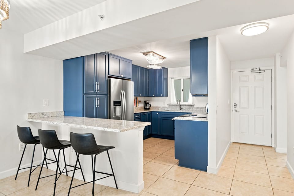 Sandy Key 411- Sleek blue cabinetry and natural light create an elegant, inviting kitchen. Three modern bar stools perfect for casual gatherings and morning coffee moments.
