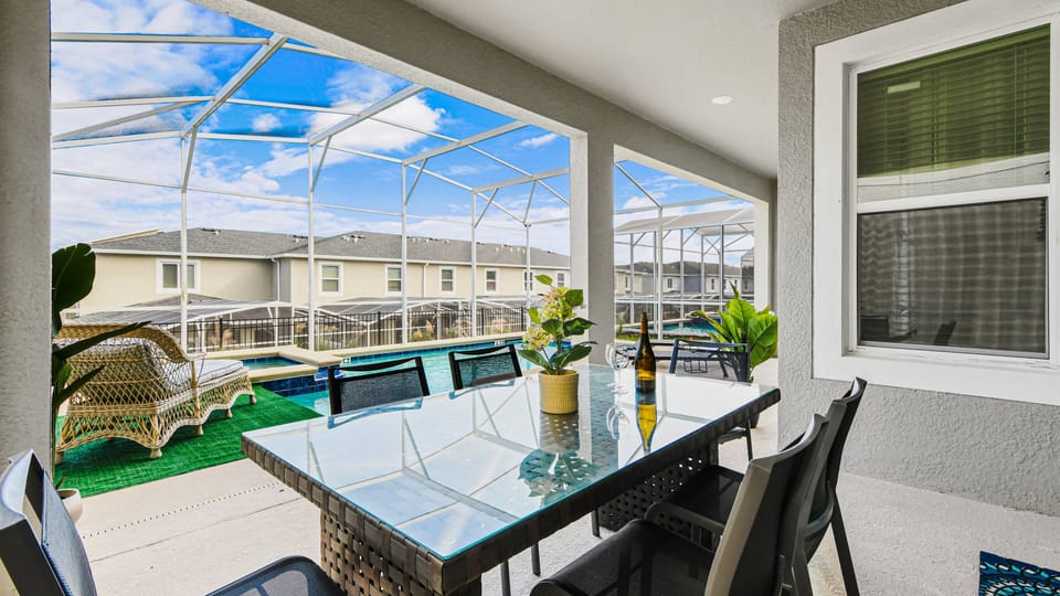 Poolside screened patio with glass dining table, lounge chairs, and sunny views.
