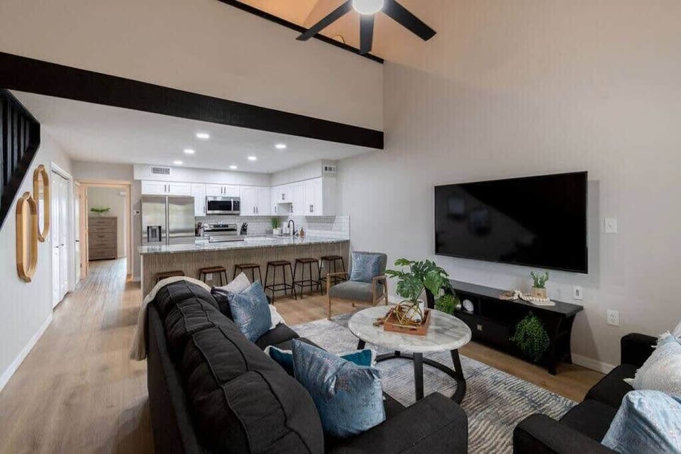Modern open-concept living room with a large flat-screen tv and kitchen bar seating.