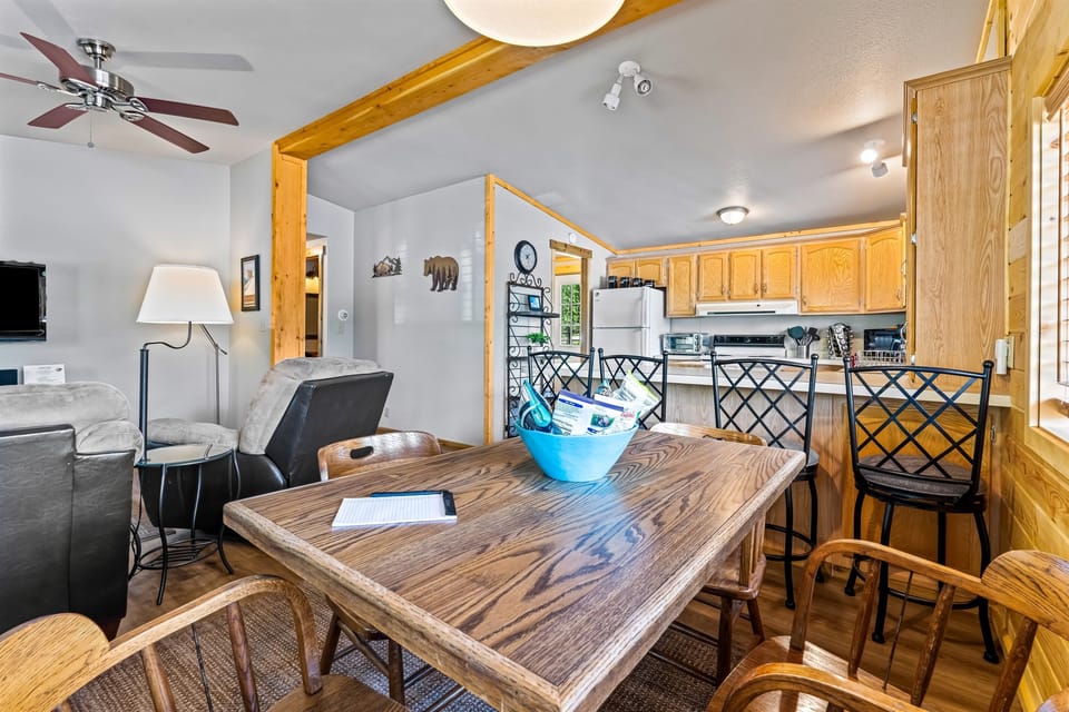 Savor moments around the dining table in the Ponderosa Pine cabin, as it elegantly connects with the living room, kitchen, and hallway in the background, creating a harmonious and stylish foca