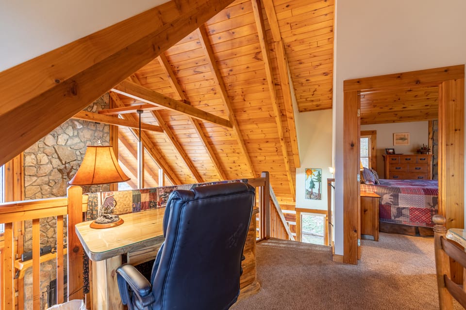 A cozy loft nook with soaring timber beams and a stone accent wall, perfect for unwinding or getting a little work done at Ambleside.