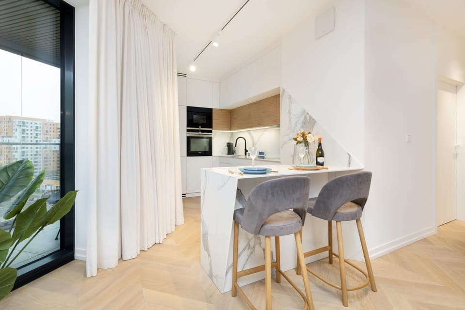 A dining area adjacent to a kitchen with a table set for two and a view of an outdoor balcony.