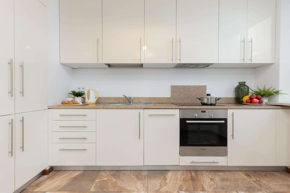 A fully equipped kitchen with white cabinets, an oven, and a countertop adorned with plants and utensils.