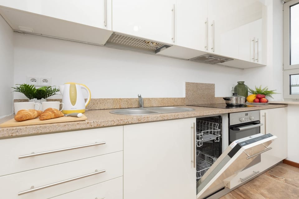 A fully equipped kitchen with white cabinets, an oven, and a countertop adorned with plants and utensils.