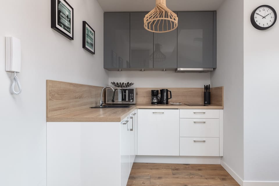 A modern, minimalist kitchen with white cabinetry, wood-textured countertops, and sleek appliances.