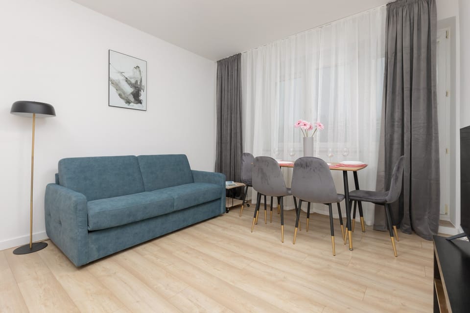 A modern living room with a blue sofa and dining area. Elegant wall art and curtains add a stylish touch.