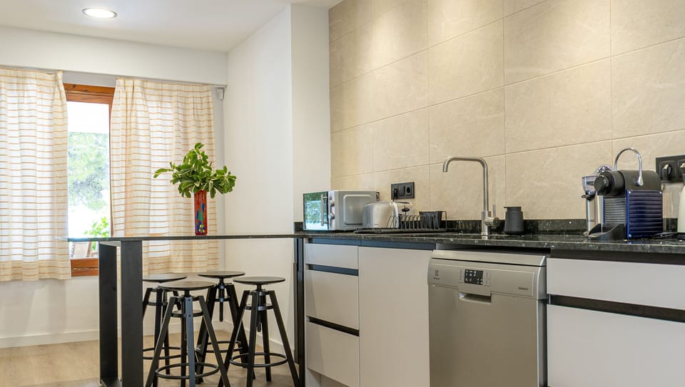 Modern kitchen equipped with dishwasher, coffee machine, toaster and breakfast bar with stools.