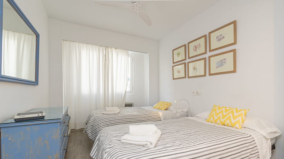 Bedroom with two single beds, yellow cushions and wall decoration.
