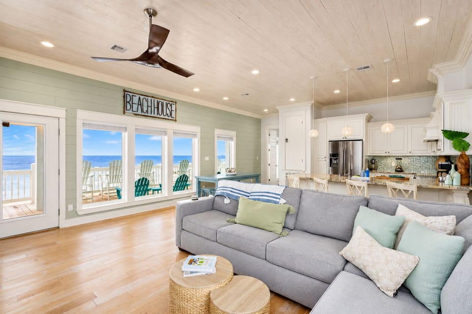 Bright open-concept living room with plush seating, coastal décor, ceiling fan, and direct balcony access with beautiful beachfront views.