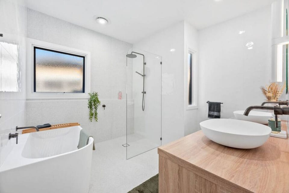 Indulge in a spa-like experience in this elegant bathroom featuring a freestanding tub, walk-in rain shower, double vanities, and serene natural finishes