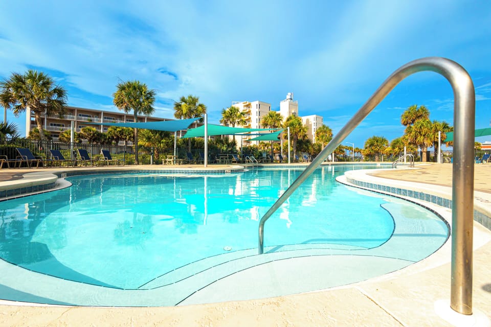 Inviting turquoise pool waters await you under bright Florida skies, framed by swaying palms and shaded lounging areas—your perfect spot to unwind in the sun.