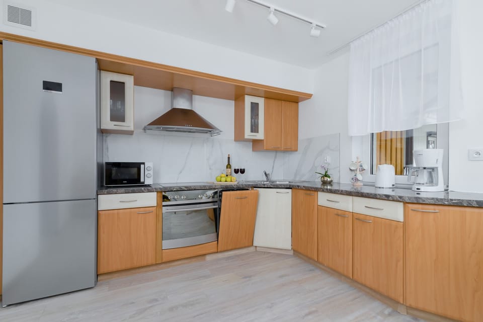A fully equipped kitchen with light wood cabinets, white countertops, and modern appliances, connected to the dining area.