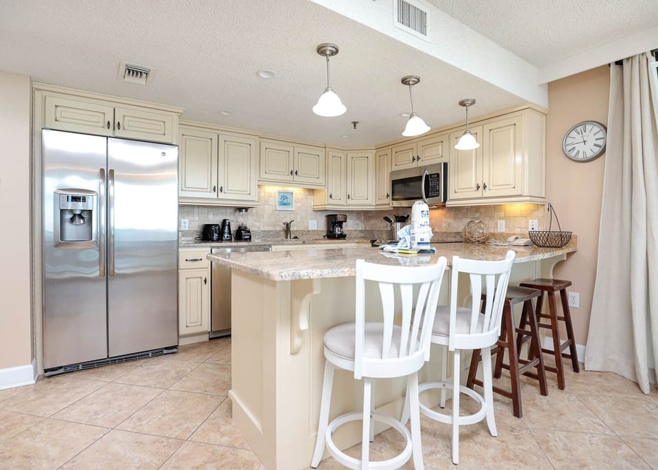 The well-equipped kitchen features light cabinetry, granite countertops, and a breakfast bar with two stools
