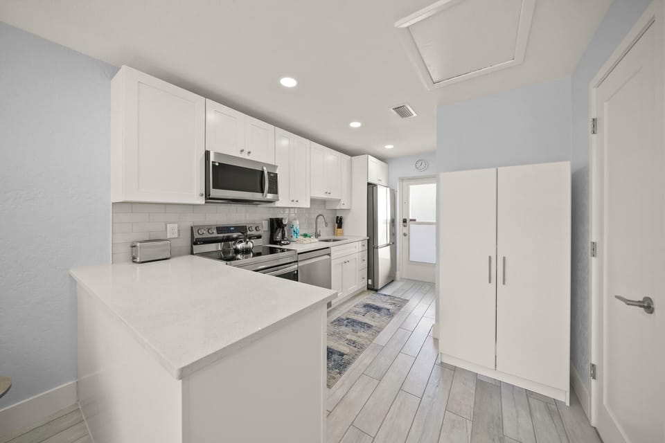 Your pristine kitchen awaits with gleaming white cabinets, stainless appliances, and a spacious island perfect for morning coffee or meal prep.