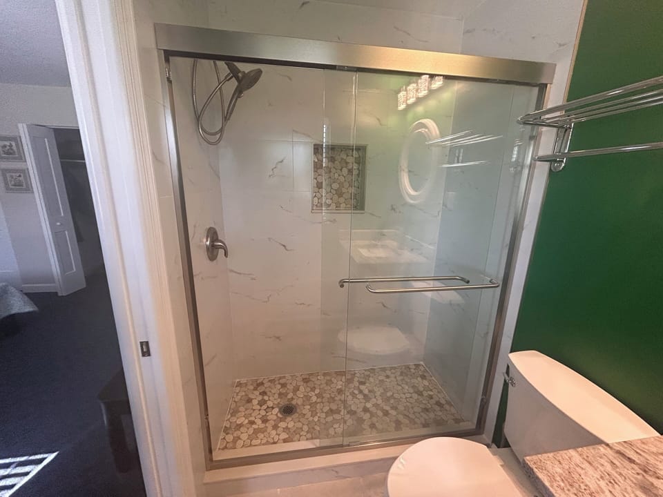 Step into your spacious glass-enclosed shower with elegant marble-look walls and mosaic tile flooring for a refreshing start to your day.