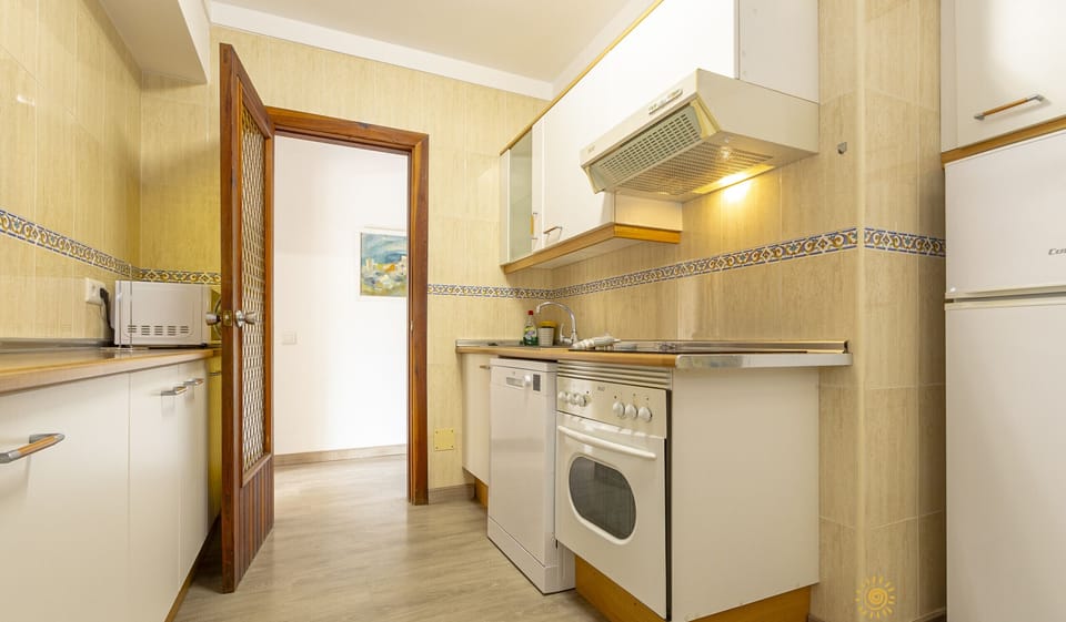 Separate kitchen with white cabinets and wooden worktop, oven and hob, extractor hood, dishwasher, microwave, sink and fridge. Tiled walls with border and wooden door to the hall.