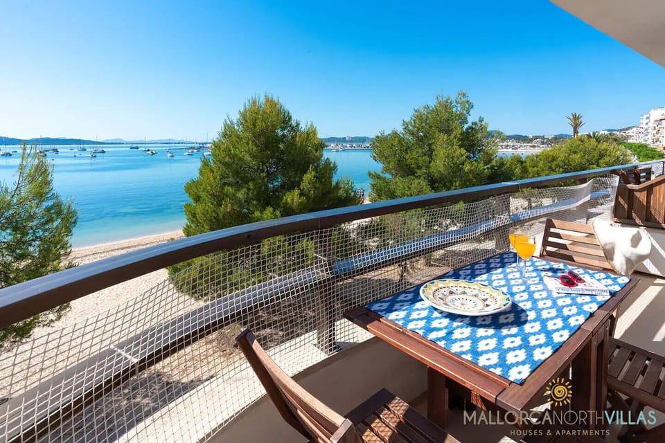 Terraza frente al mar con mesa, sillas y espectaculares vistas a la playa, los pinos y la bahía desde nuestro apartamento de vacaciones en Mallorca.