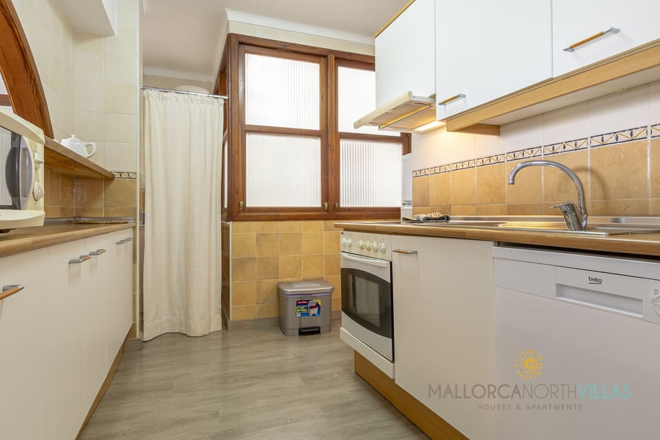 Bright and functional kitchen with white cabinets, wooden countertop, oven, dishwasher and a large window that brings in natural light, along with practical storage and essential appliances.
