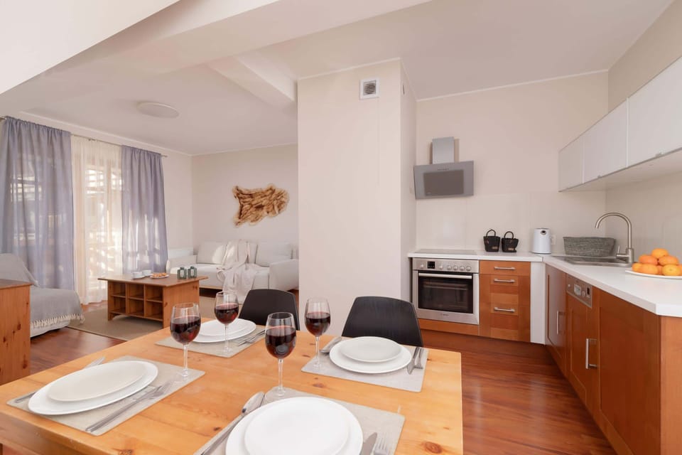 A spacious living area with wooden flooring, modern furniture, and large windows for a bright atmosphere.