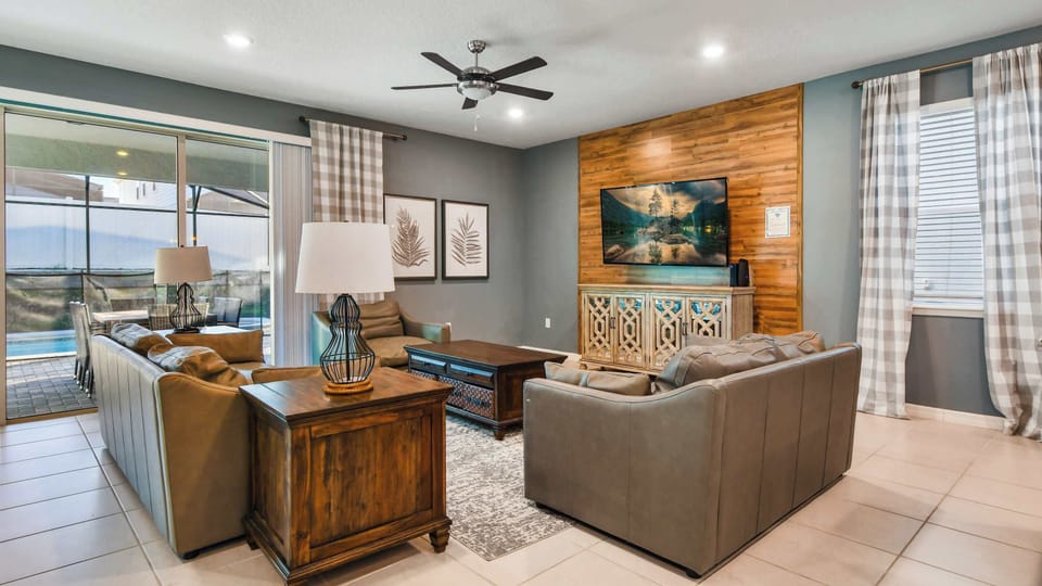 Cozy living area with plush leather seating, rustic accents, large TV, and poolside patio access.